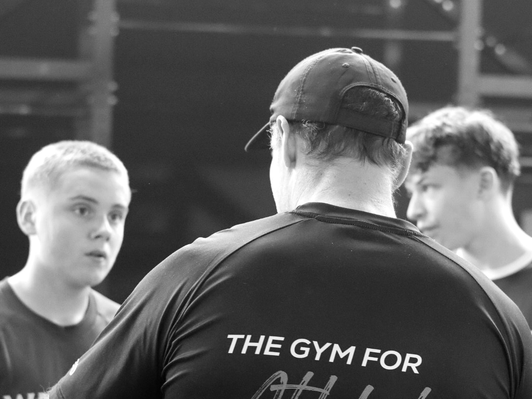 Bryan back to camera coaching young athletes inside the Nth Degree gym; 'Gym for Athletes' shirt visible.